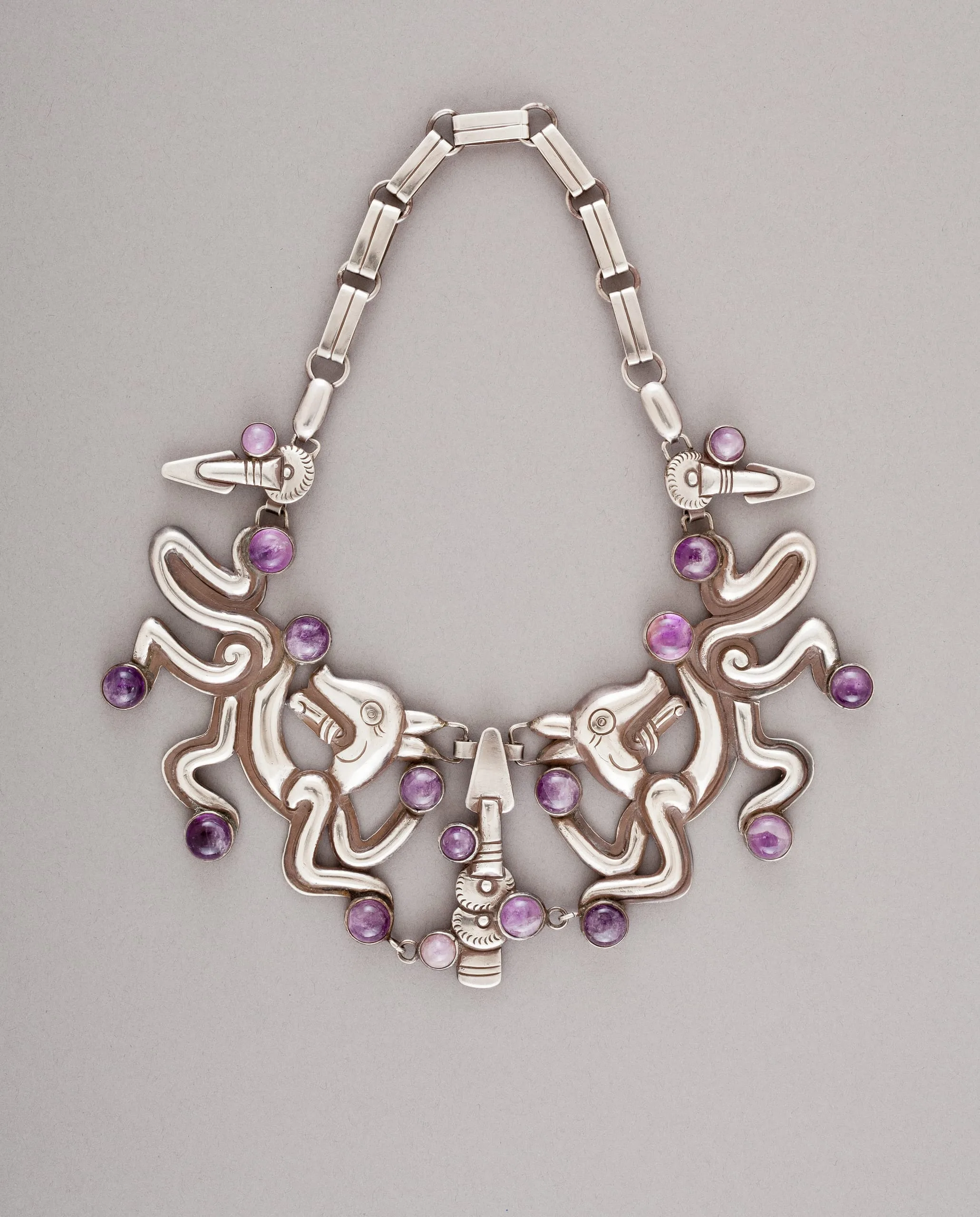 Silver necklace of paired stylized serpents set with amethyst cabochons, on a rectangular link chain, by William Spratling