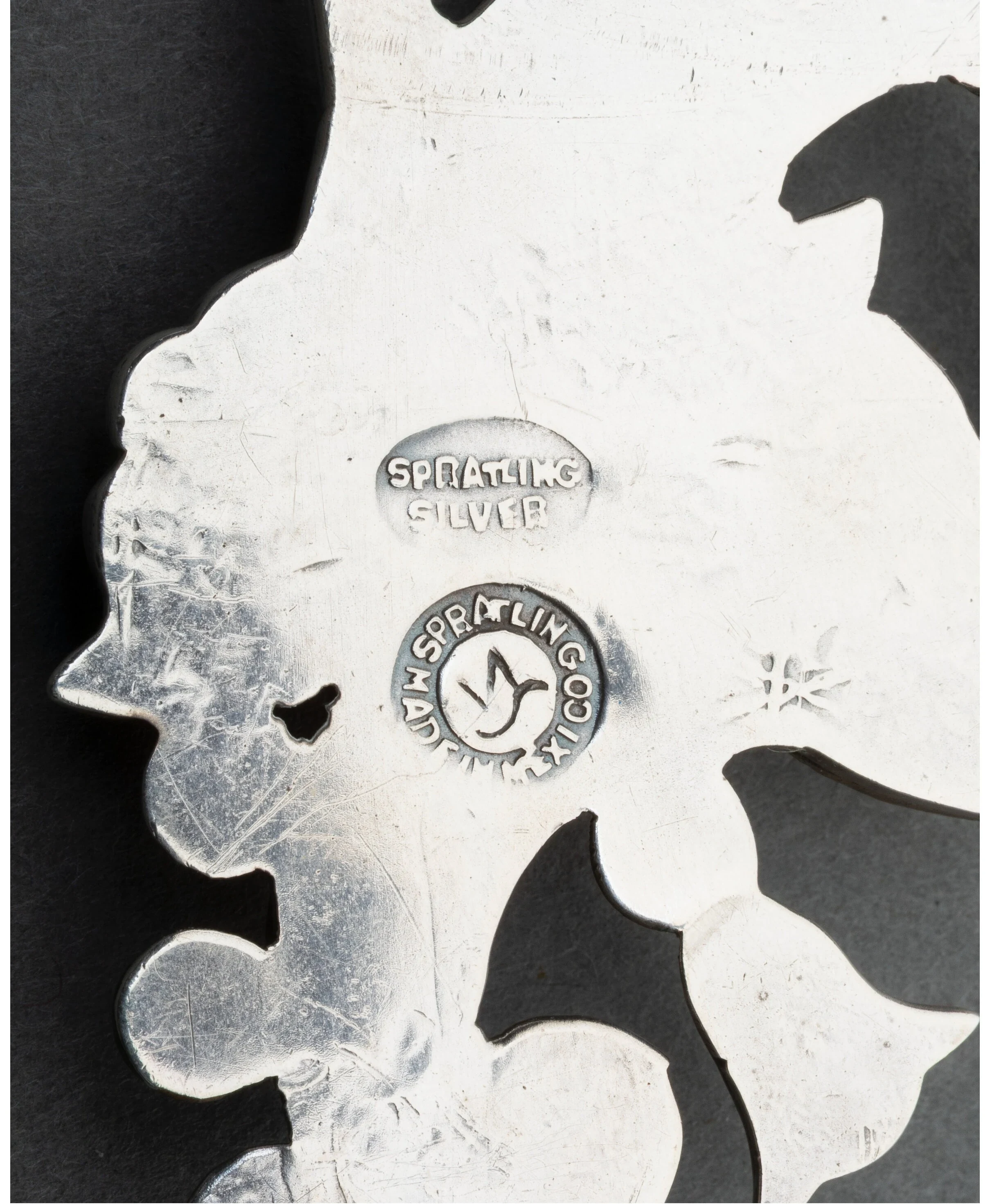 Reverse of a pierced silver brooch showing two stamped marks: an oval SPRATLING SILVER stamp above a circular SPRATLING MADE IN MEXICO mark enclosing a bird glyph